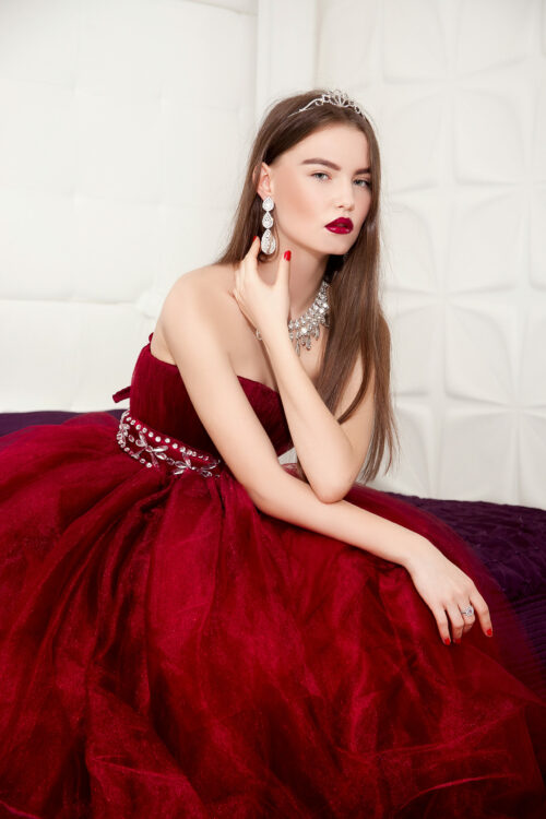 A girl in a chic Marsala ball gown against the background of a light interior.