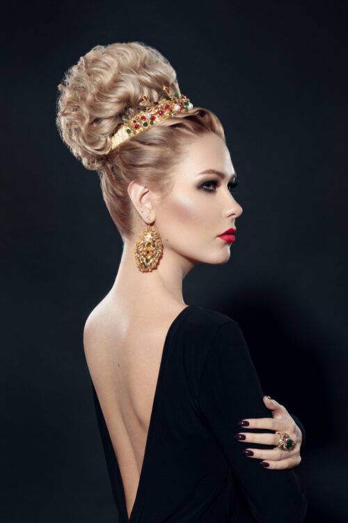 Rear view of a stylish blonde young woman with hairdressing, makeup, over black background.